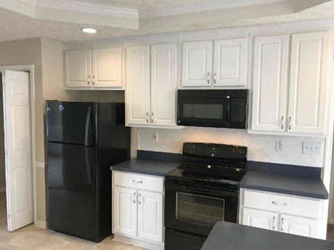 A black refrigerator and oven in a kitchen with white cabinets.