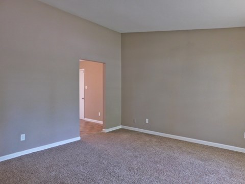 an empty living room with carpet and a door to a hallway