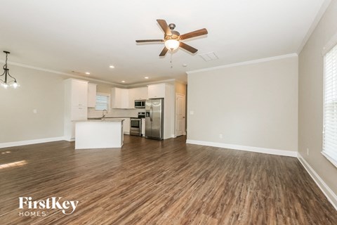 an empty living room with a ceiling fan and a kitchen