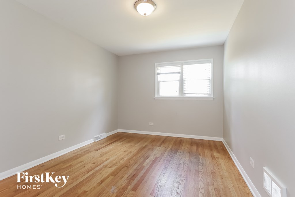 a bedroom with white walls and wood flooring and a window