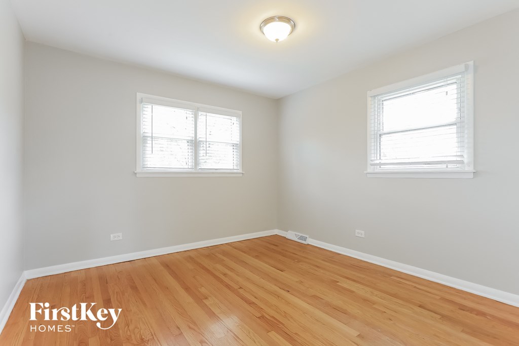a bedroom with a hardwood floor and two windows