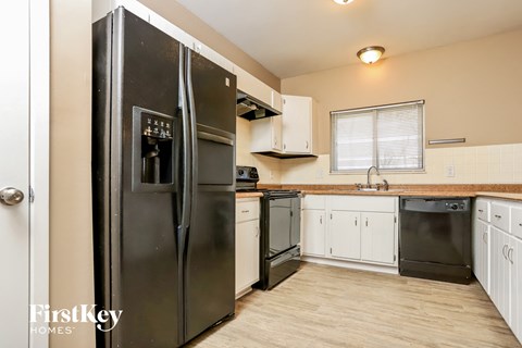 A black refrigerator is in a kitchen with wooden floors and white cabinets.