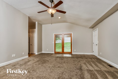 an empty living room with a ceiling fan and a door to the backyard