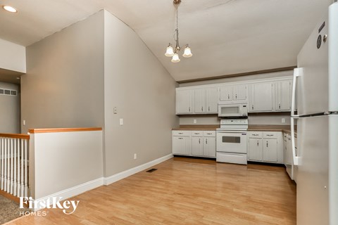 an empty kitchen with white cabinets and appliances and a wooden floor