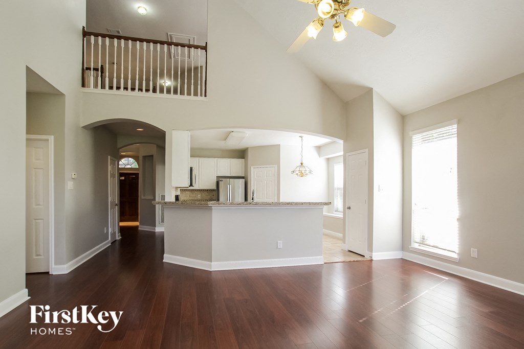 an empty living room with a kitchen and a ceiling fan