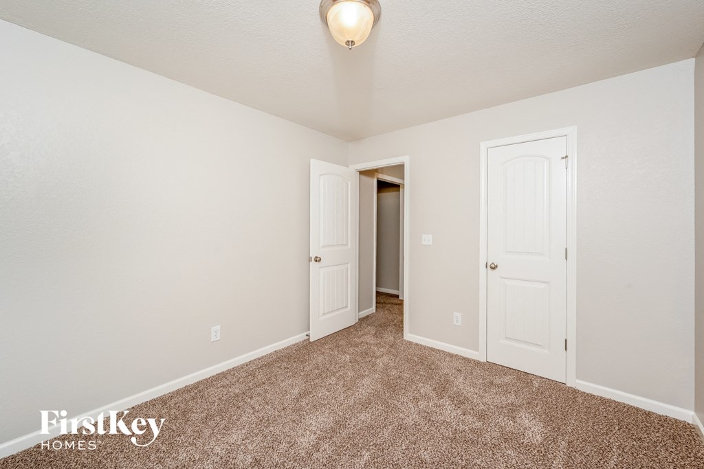 a bedroom with white walls and carpet and a door to a closet