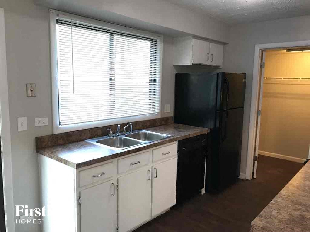 A kitchen with a black refrigerator, white cabinets, and a granite countertop.