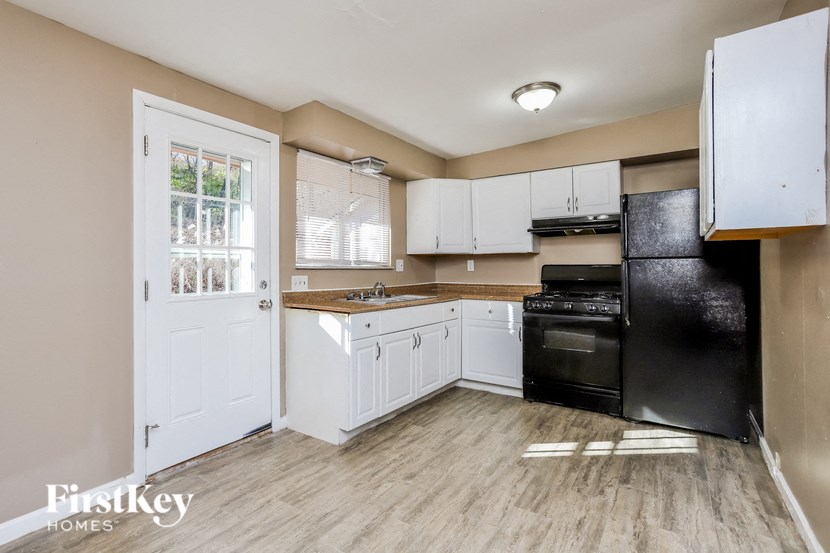 A kitchen with a black refrigerator, white cabinets, and a wooden floor.
