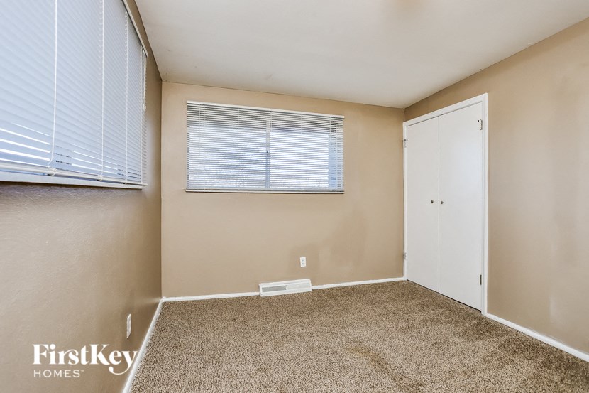 A room with a carpeted floor, a window with blinds, and a white door.