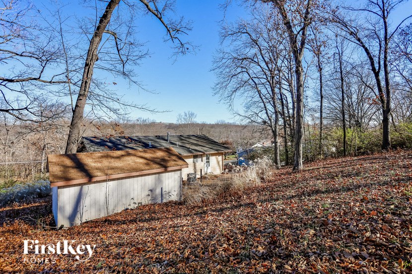 A shed sits in a field with trees and leaves on the ground.