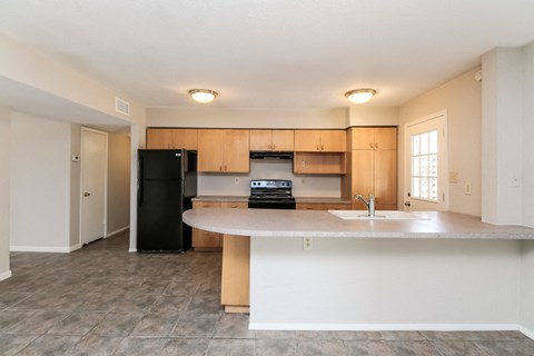 A kitchen with a black fridge, white countertops, and wooden cabinets.