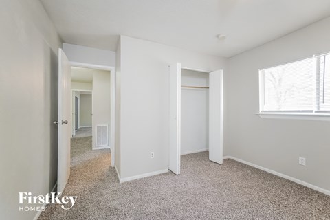 a bedroom with white walls and carpet and a door to a closet