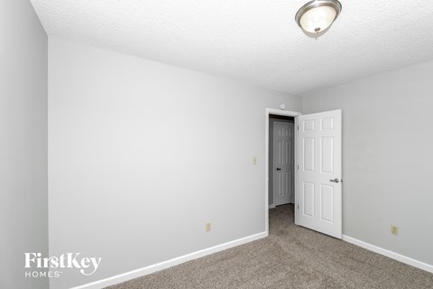 a bedroom with white walls and carpet and a door to a closet
