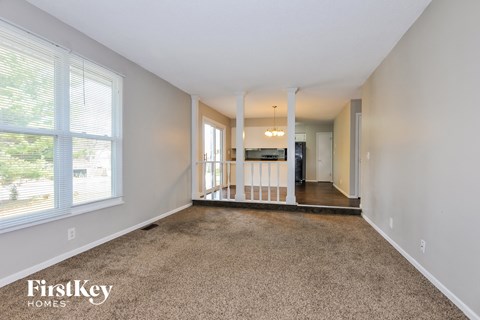 A spacious living room with a carpeted floor and a view of trees through the window.