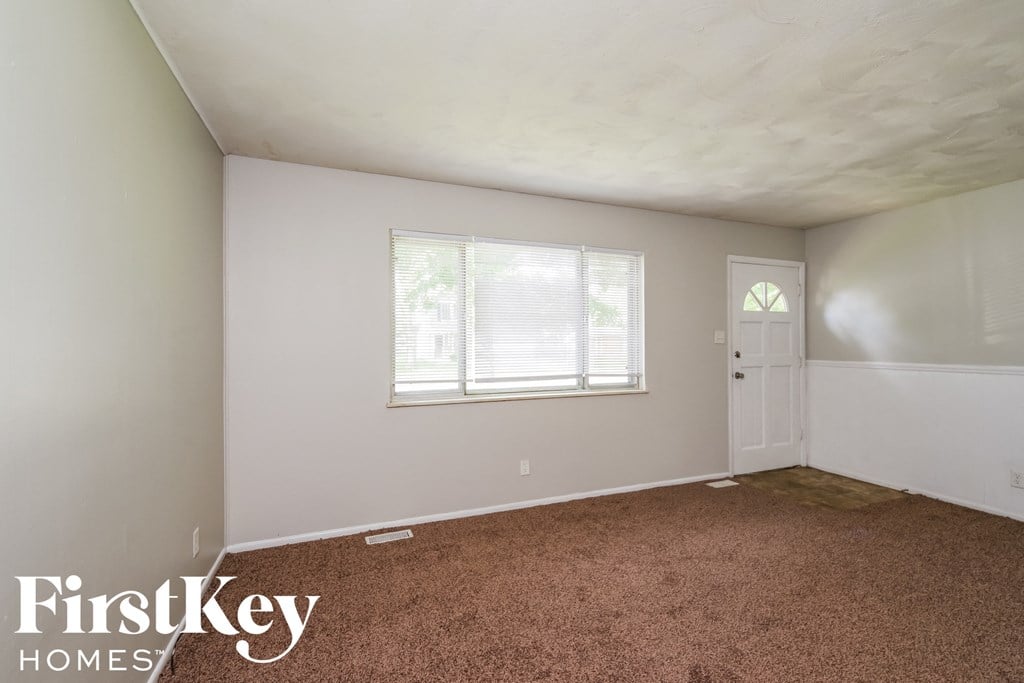A room with a carpeted floor and a window with blinds.
