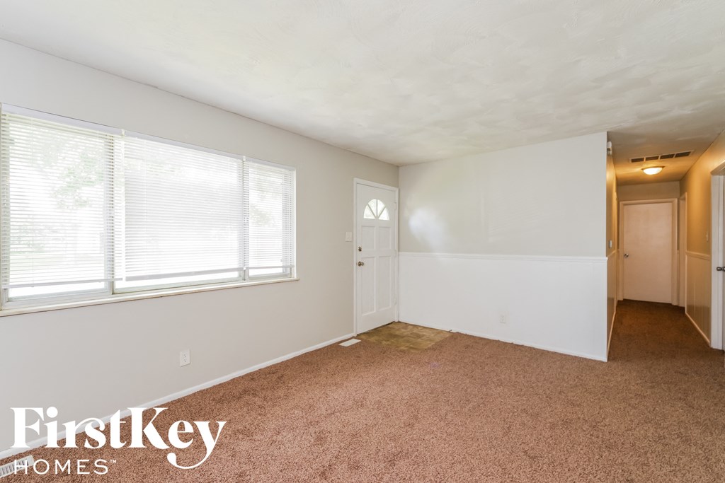 A carpeted room with a window and a door leading to another room.