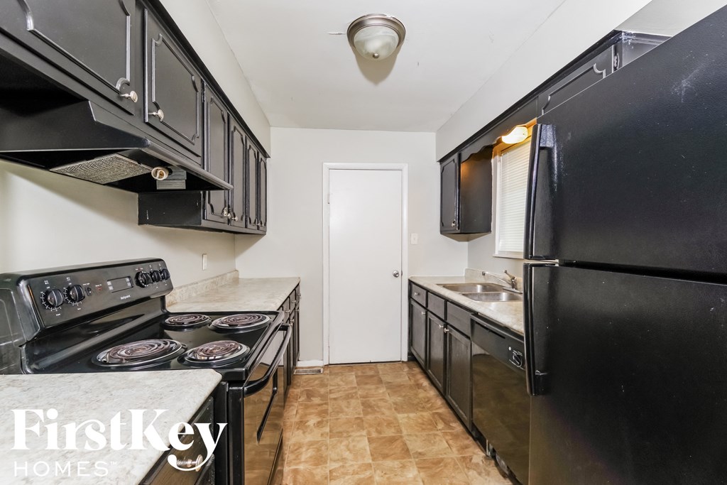 A kitchen with black appliances and a white door in the background.