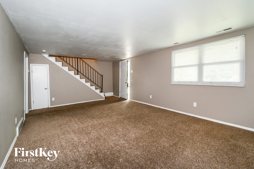 the living room of an empty house with carpet and a staircase