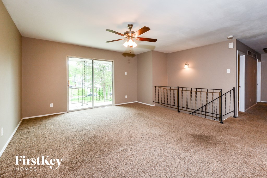 an empty living room with a ceiling fan and a balcony
