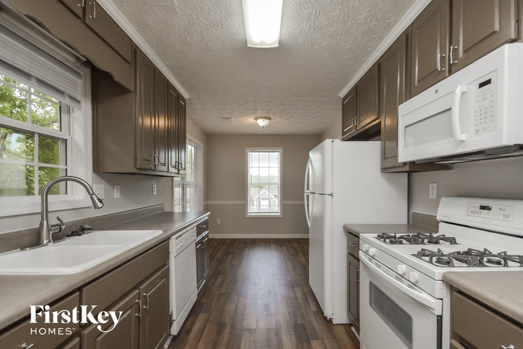 an empty kitchen with white appliances and wooden floors