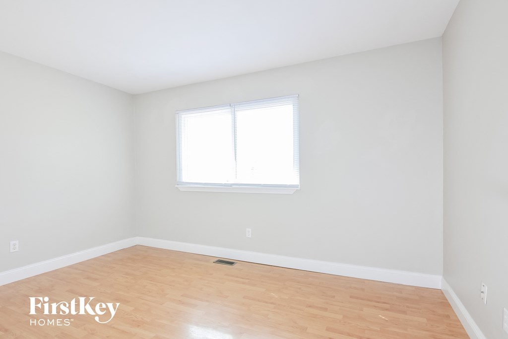 a bedroom with white walls and wood floors and a window