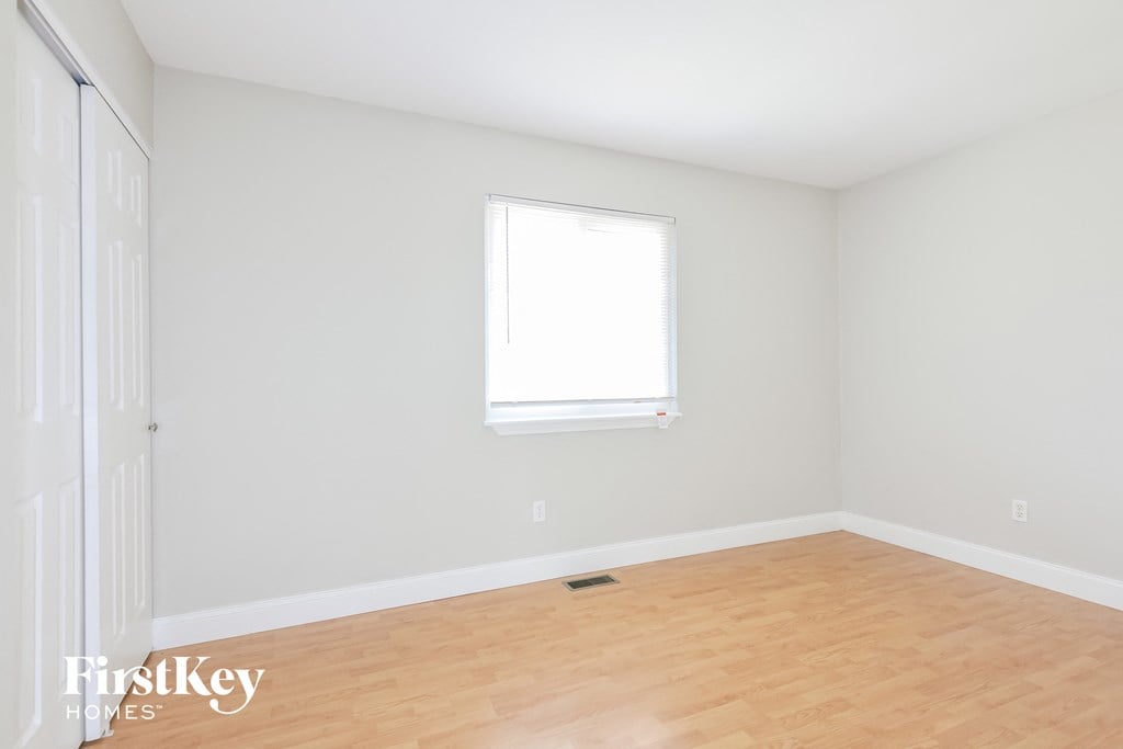 a bedroom with white walls and wood floors and a window