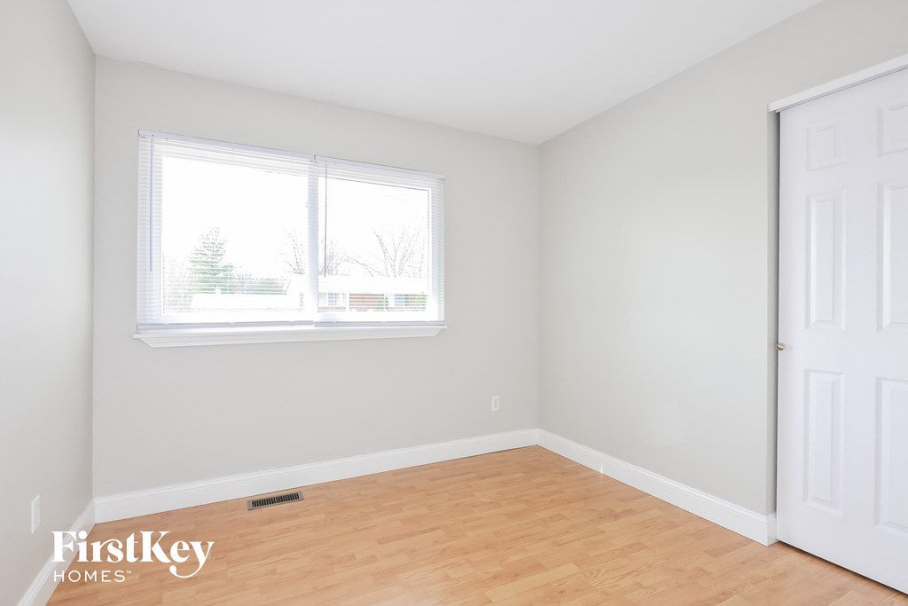 a bedroom with white walls and wood floors and a window