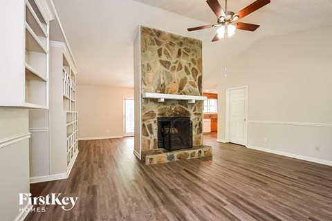 A spacious living room with a stone fireplace and wood flooring.