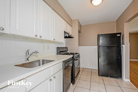 A kitchen with white cabinets and a black refrigerator.