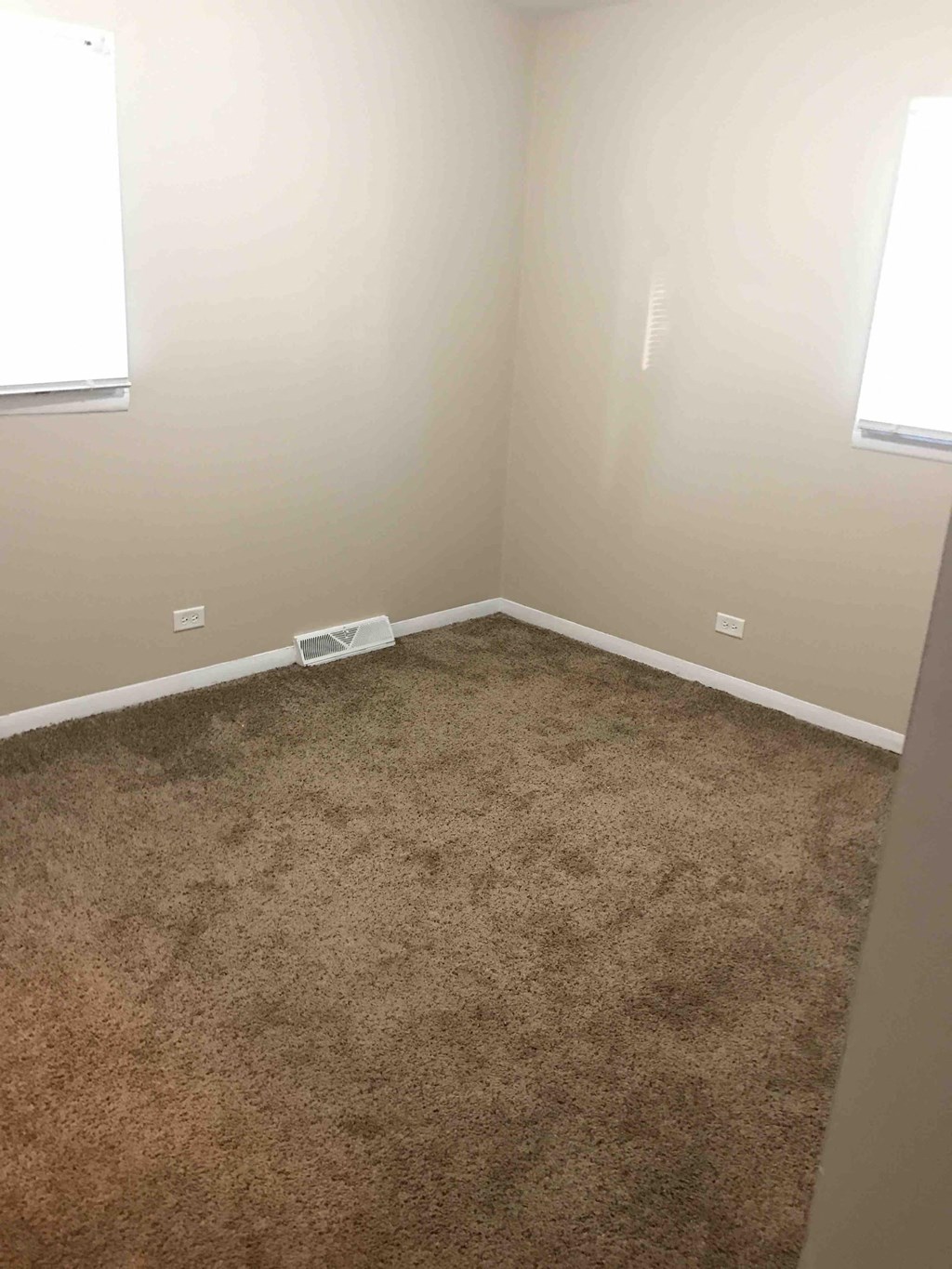 a room with a carpeted floor and two windows