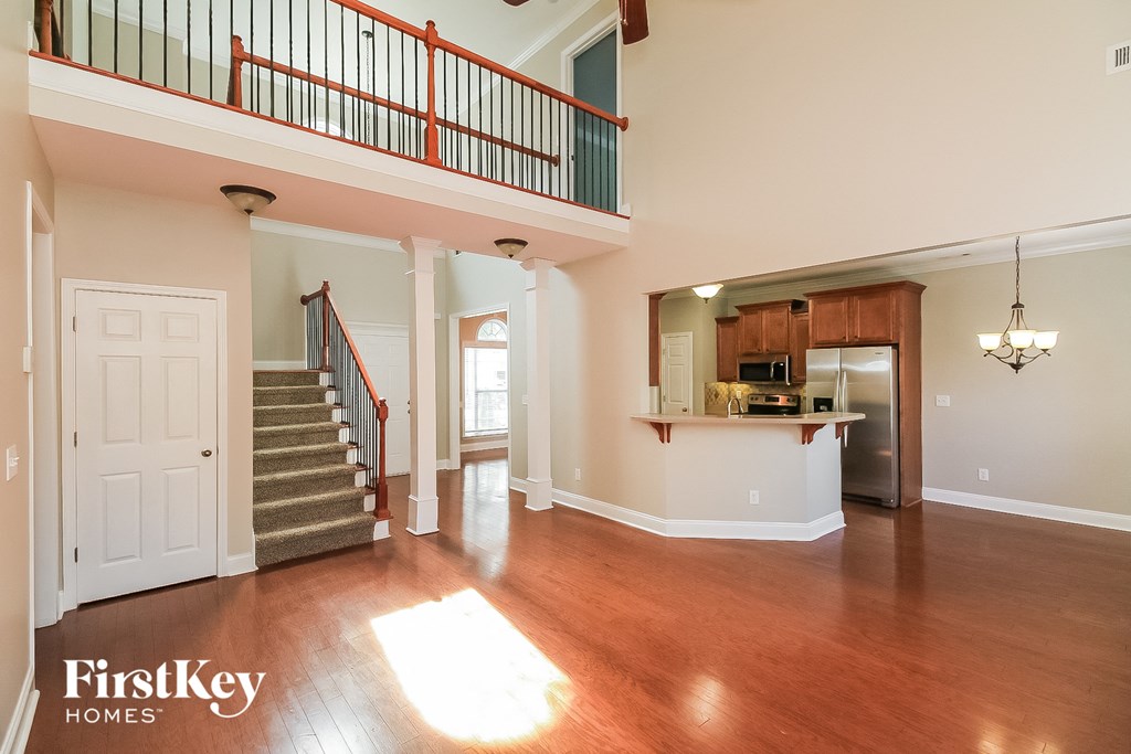 A spacious living room with wood floors and a staircase with red railings.