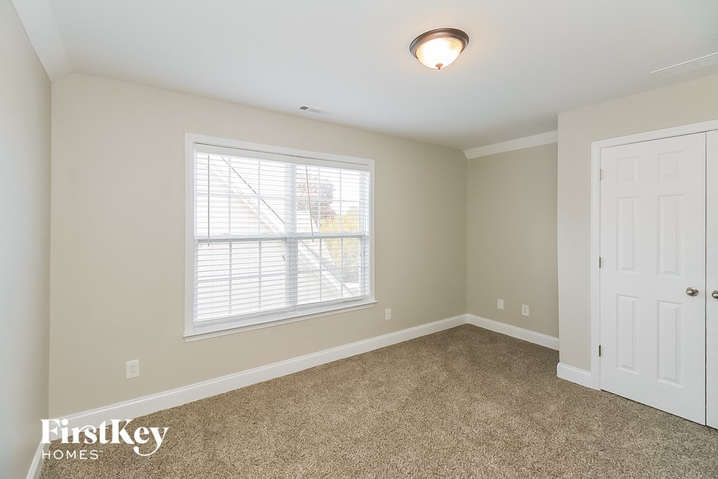 A room with a carpeted floor, a window with blinds, and a white door.