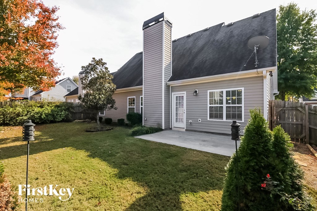 A house with a grey roof and a white door is surrounded by a green lawn.