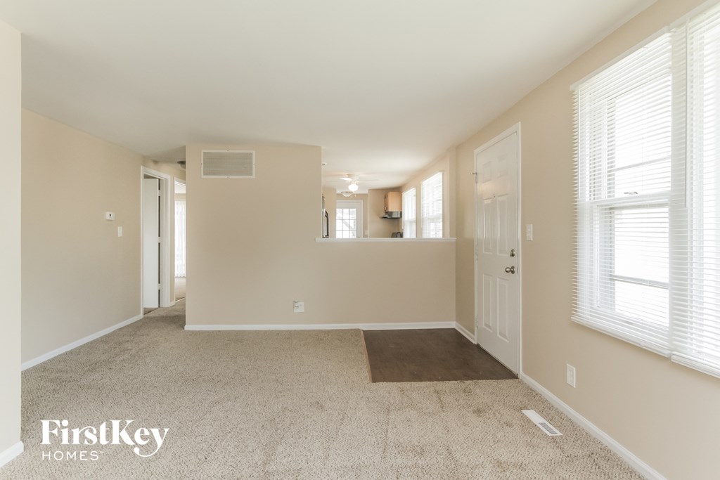 A spacious room with a carpeted floor and a window with blinds.