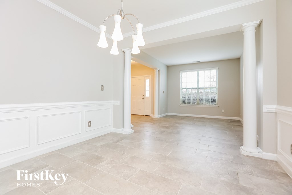 A spacious room with a chandelier and a window with blinds.