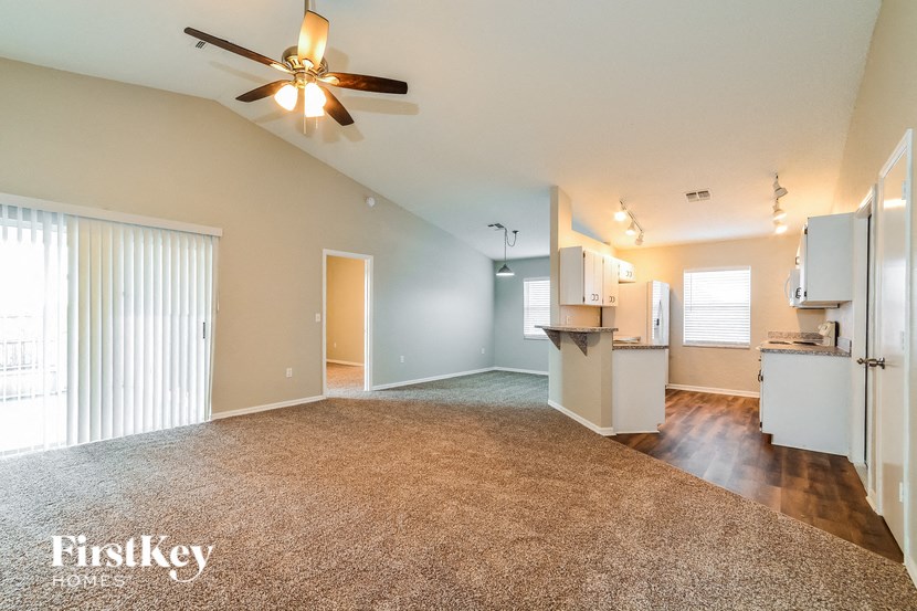 A spacious living room with a ceiling fan and a carpeted floor.