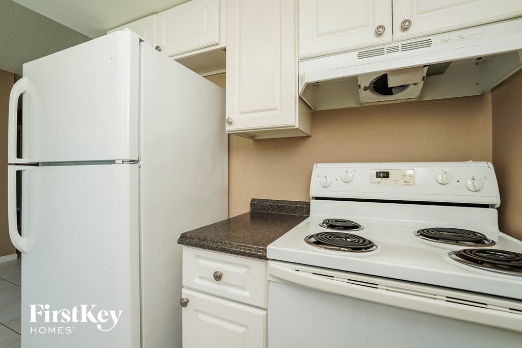 A white refrigerator is in a kitchen with a stove and cabinets.