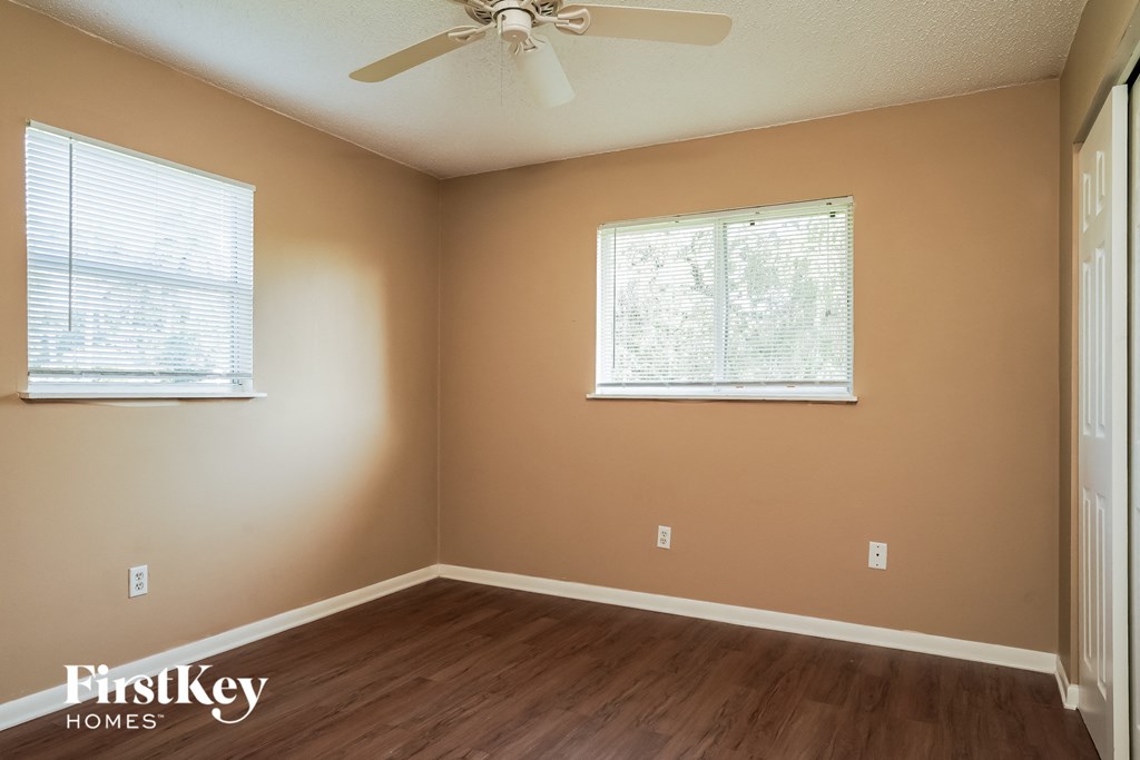 A room with a ceiling fan and two windows.