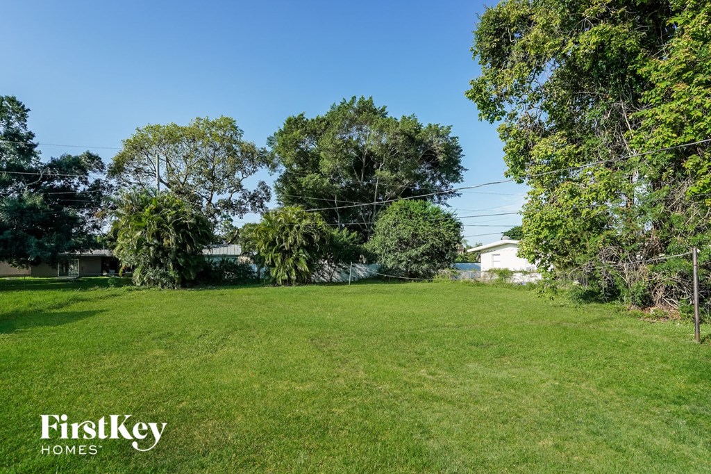 A grassy field with trees and a house in the background.