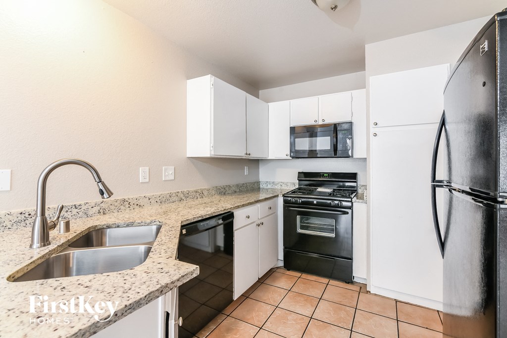 A kitchen with a black refrigerator and white cabinets.