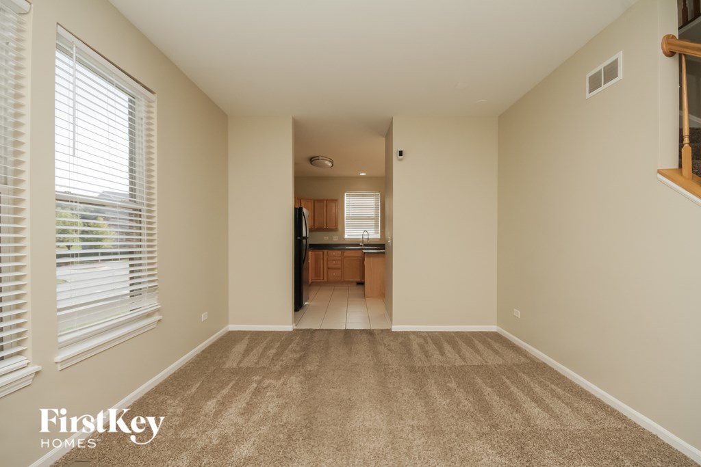 A carpeted room with a kitchen in the background.