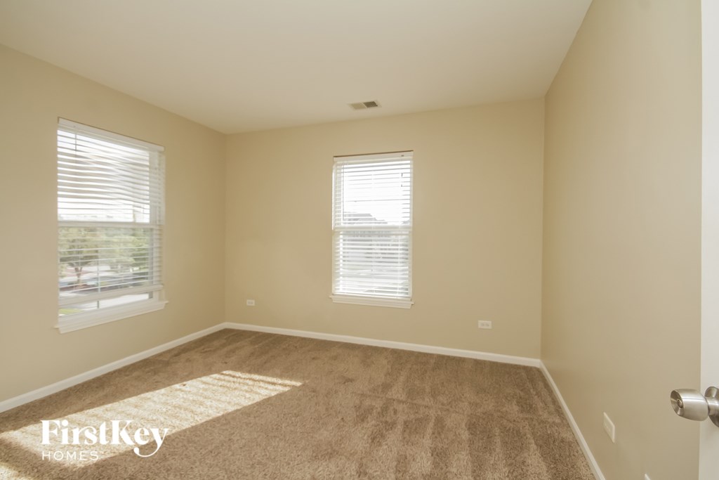 A room with a carpeted floor and two windows.