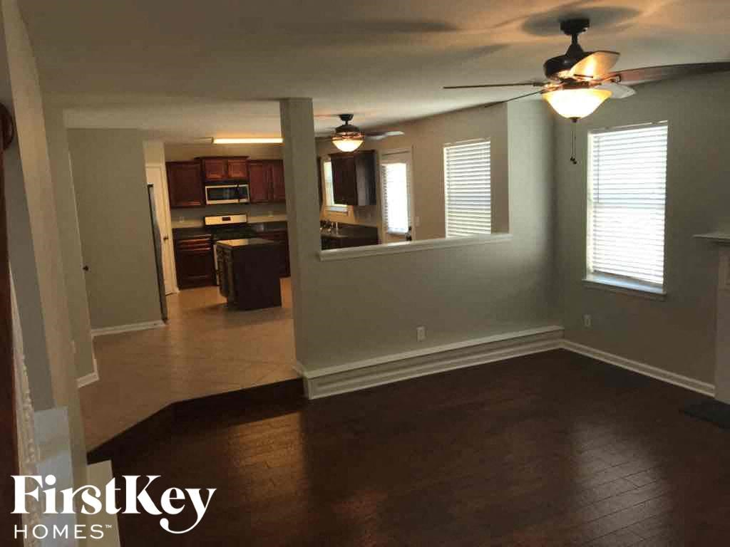 an empty living room with a ceiling fan and a kitchen