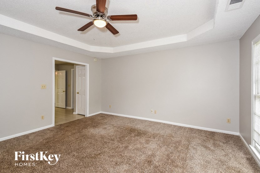 A carpeted room with a ceiling fan and a doorway leading to another room.