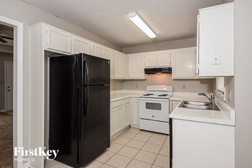 A black refrigerator in a kitchen with white cabinets.