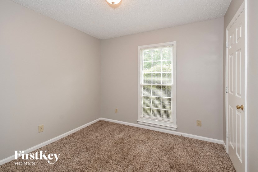 A room with a carpeted floor, a window with blinds, and a door.