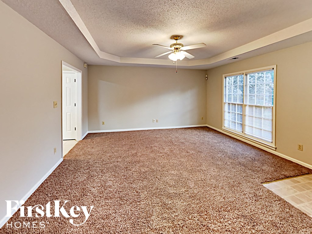 A carpeted room with a ceiling fan and a window.