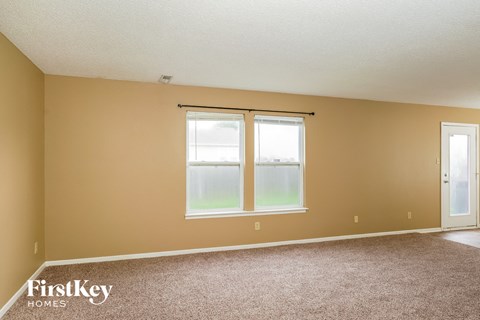 A room with a carpeted floor, a window with a view of a grassy field, and a door.