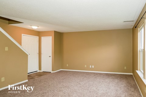 A room with a carpeted floor and a staircase on the left side.