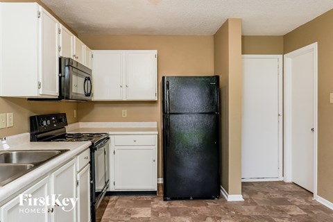 A kitchen with a black fridge, white cabinets, and a stainless steel sink.